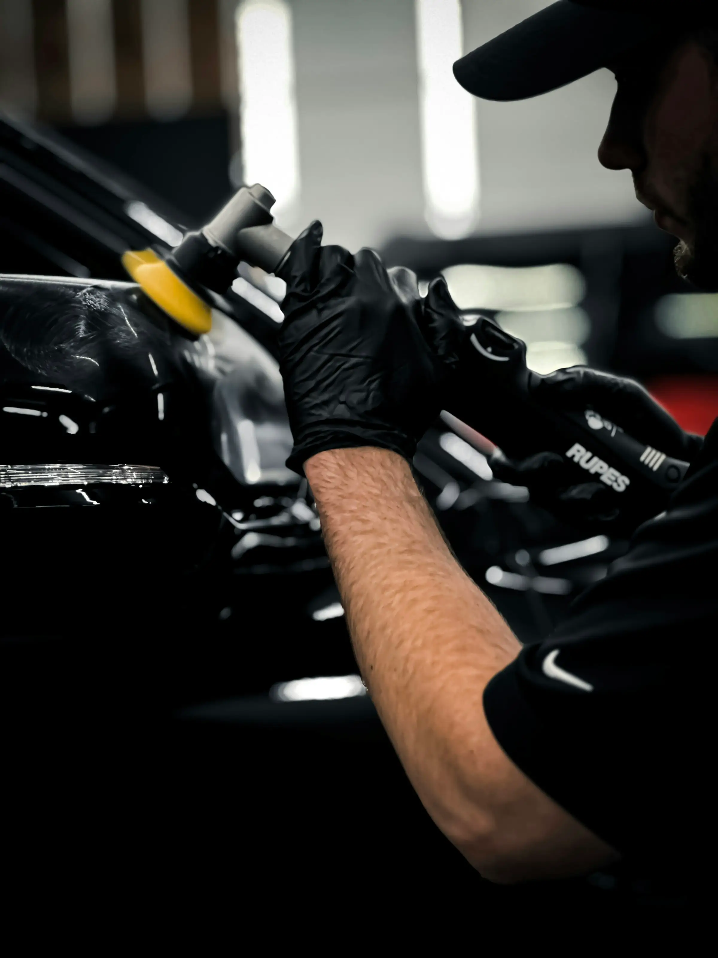 Detailer werkt met een polijstmachine aan een donkere carrosserie