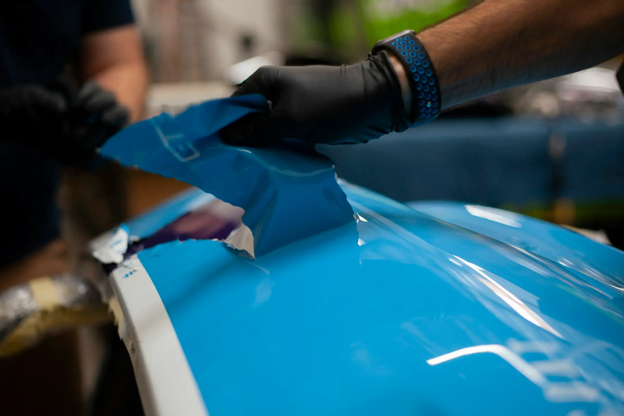 Blauwe folie wordt met een rakel op de motorkap aangebracht